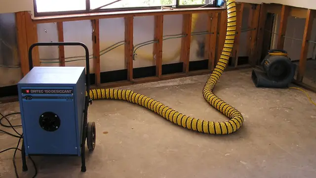 Dehumidifier with a yellow duct drying a room with the lower wall opened up